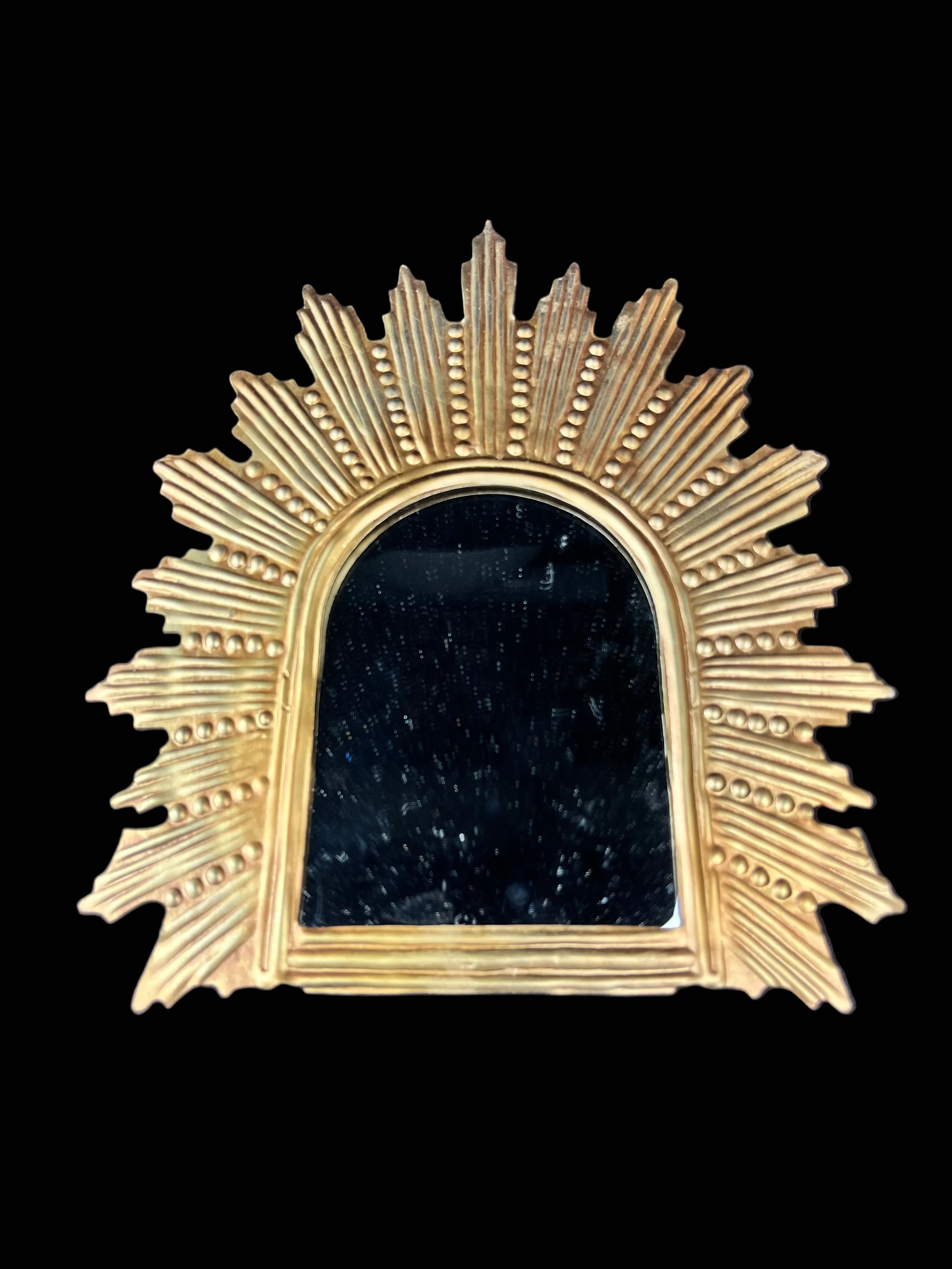 Decorative gold mirror with sunburst design on a dark blue background