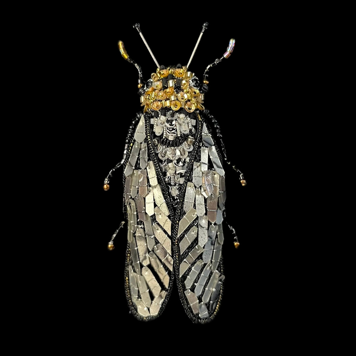 A highly detailed, handcrafted cicada insect brooch or pin, featuring intricate silver and gold metallic wing-like patterns, black beadwork, and a gold-embellished head, displayed on a black velvet background.