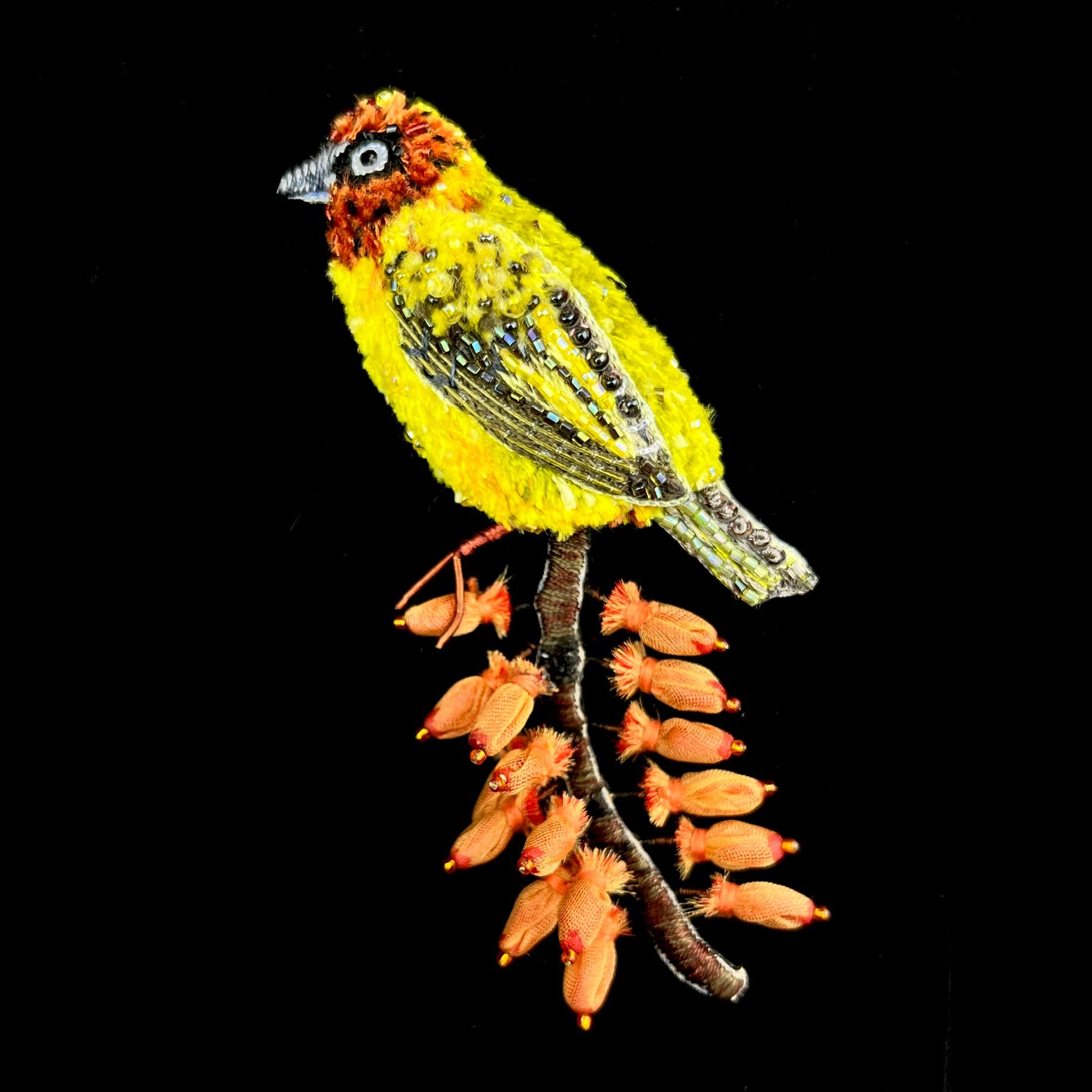A bright yellow bird stands perched on top of a brown stick with iron colored berries which match the color of the birds head.
