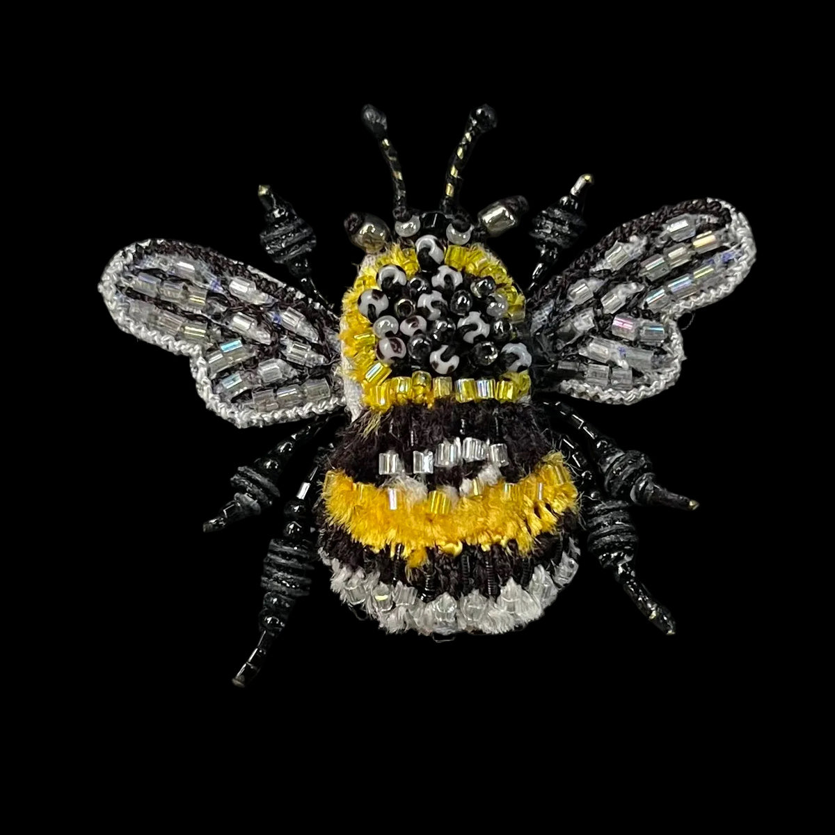 A detailed beaded bumblebee brooch featuring black, yellow, and silver iridescent beads on a solid black background.