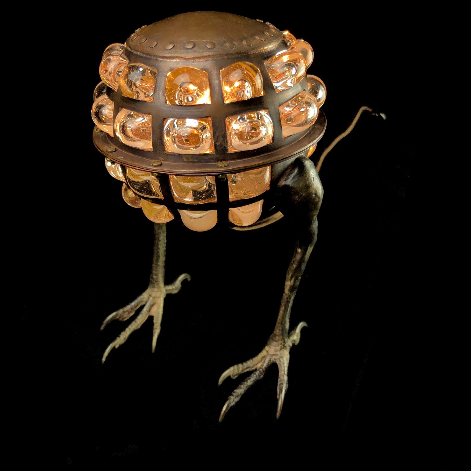 A desk lamp with a spun copper body, cast bronze hawk feet, and clear blown glass shade.